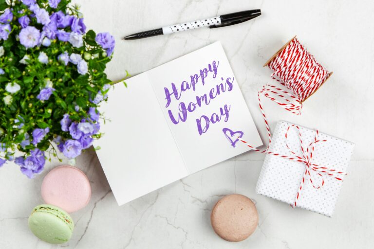 Celebrate Women's Day with a thoughtful greeting card, flowers, macarons, and a wrapped gift on a white background.