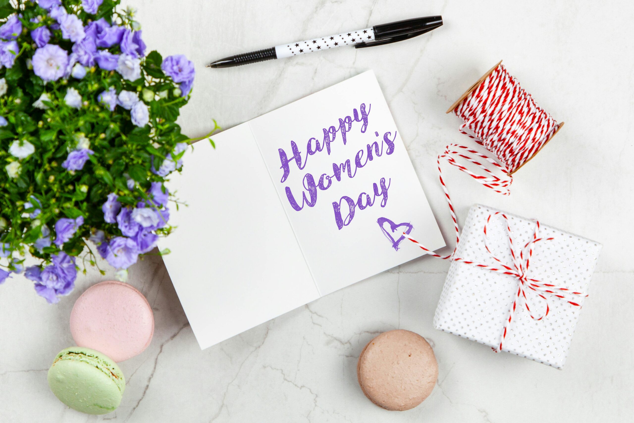 Celebrate Women's Day with a thoughtful greeting card, flowers, macarons, and a wrapped gift on a white background.